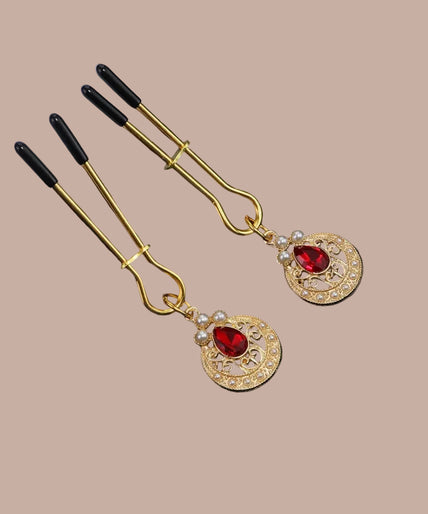 Liebe Seele – Sieraden-tepelklemmen – Goud Gold-tone nipple clamps with black tips, red teardrop stones and pearl-like circular pendants, front view.