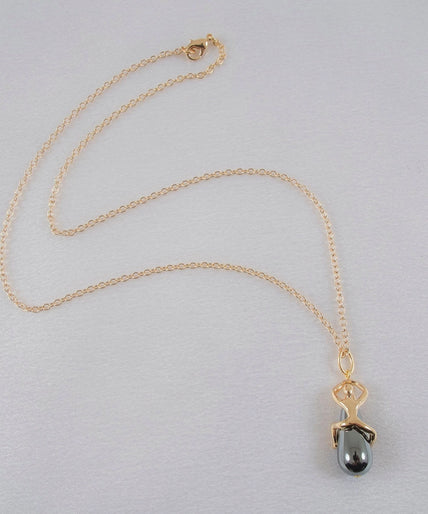 Sylvie Monthulé – Secret Passion Hematite Pearl Pendant Gold Sylvie Monthulé Secret Passion pendant with a gold-coloured figure around a dark teardrop bead on a fine chain.