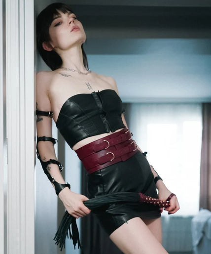 Flogger with black falls, wine-red studded handle and wrist loop, curved arrangement.