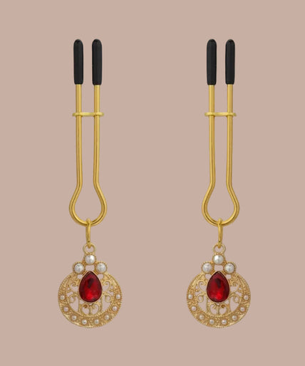 Gold-tone nipple clamps with black tips, red teardrop stones and pearl-like circular pendants, front view.