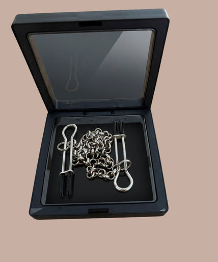 Silver-tone U-shaped nipple clamps with black tips and connecting chain inside an open black display box.