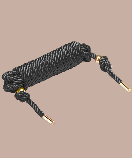 Coiled Liebe Seele black shibari rope with knotted ends and gold-coloured tips.