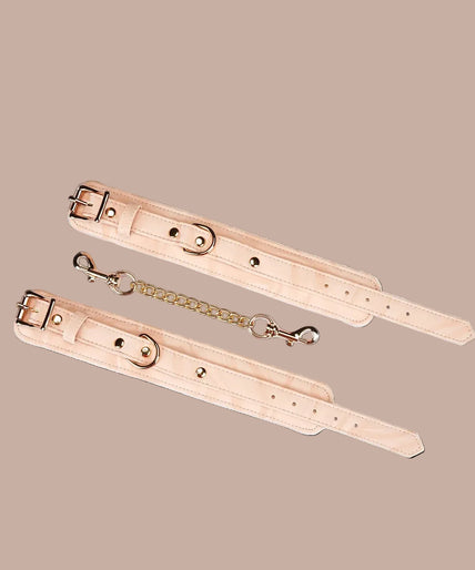Angled view of Liebe Seele Boudoir Amor blush pink wrist cuffs showing buckles, lining and connector chain.