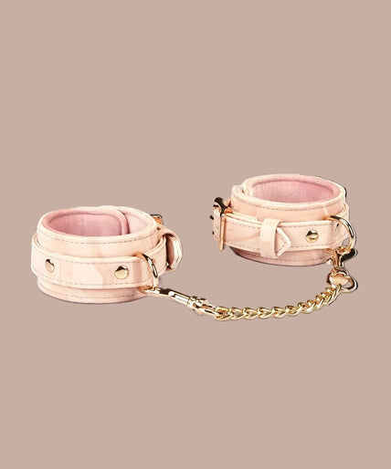 Angled view of Liebe Seele Boudoir Amor blush pink wrist cuffs showing buckles, lining and connector chain.