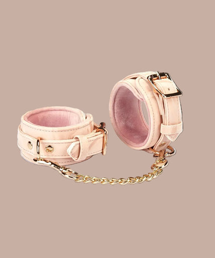 Angled view of Liebe Seele Boudoir Amor blush pink wrist cuffs showing buckles, lining and connector chain.
