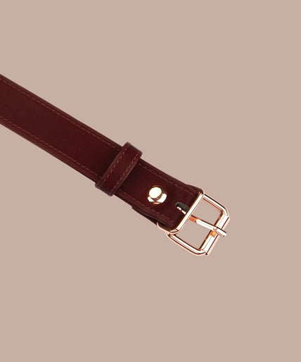 Dark red ball gag with black perforated ball, metal side rings and adjustable buckle strap, angled view.