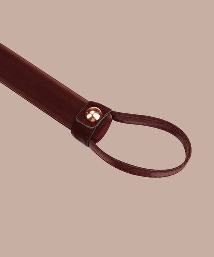 Dark red flogger with narrow falls, matching wrist loop and rose-gold-tone rivets, curved arrangement.