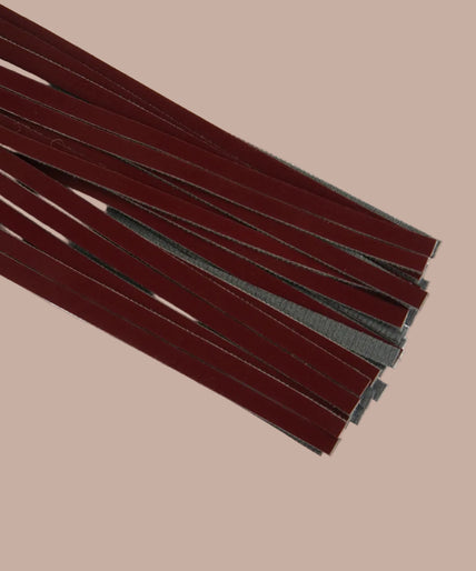 Dark red flogger with narrow falls, matching wrist loop and rose-gold-tone rivets, curved arrangement.