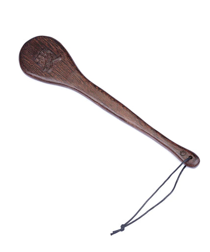 Dark wooden paddle with engraved character on rounded head and black cord wrist loop, vertical view.