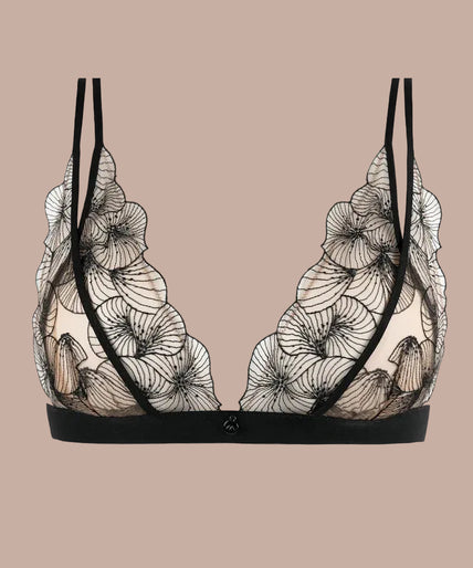 Model wearing black Menu Plaisir triangle bra with floral embroidery and matching thong, hand at her neck.