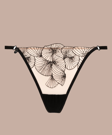 Model wearing black Menu Plaisir floral thong and matching underwire bra, one hand beside her head.