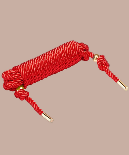 Coiled Liebe Seele red shibari rope with knotted ends and gold-coloured tips.