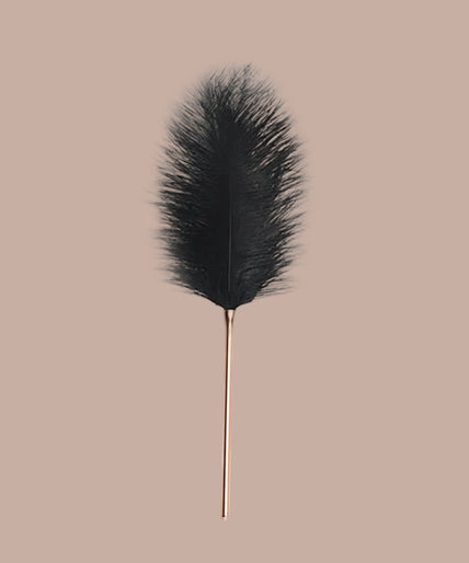 Black feather tickler with slender rose-gold-tone handle, shown vertically.