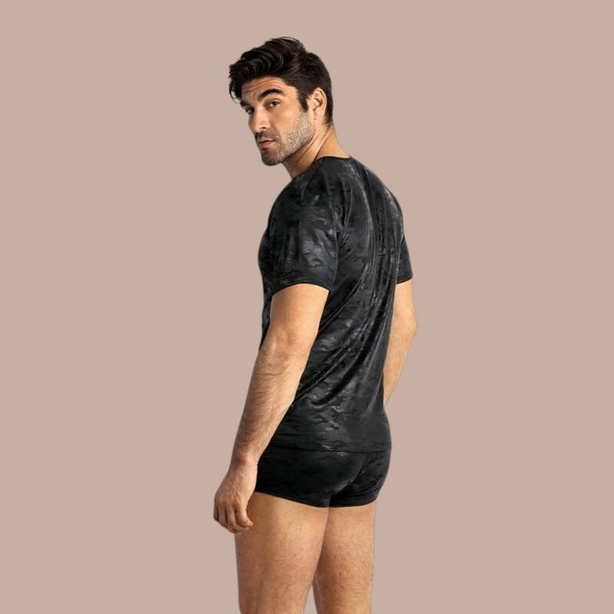 Pleasurements Anais Men Electro T-shirt in zwart met subtiel camouflagepatroon gedragen door een man op een beige achtergrond